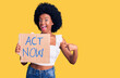 Young african american woman holding act now banner smiling happy pointing with hand and finger