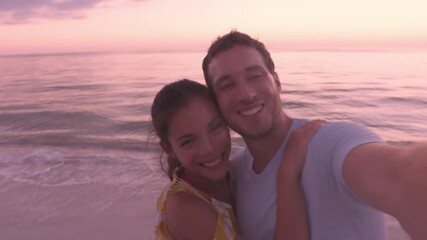 Wall Mural - Beach sunset couple relaxing on summer honeymoon vacation travel watching sunset at Lover's key, Florida near Fort Myers Beach, Man and woman taking phone selfie video.