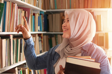 Asian muslim woman wearing hijab picking book in bookshelf, education concept, reading learning studying in library