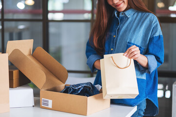 Wall Mural - Closeup image of a woman opening and looking inside shopping bag with postal parcel box of clothing for delivery and online shopping concept