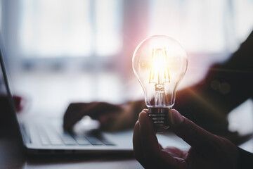 Aufkleber - hand of a man with a light bulb and he is using a notebook computer. The idea of ​​inspiration from online technology.innovation idea concept.