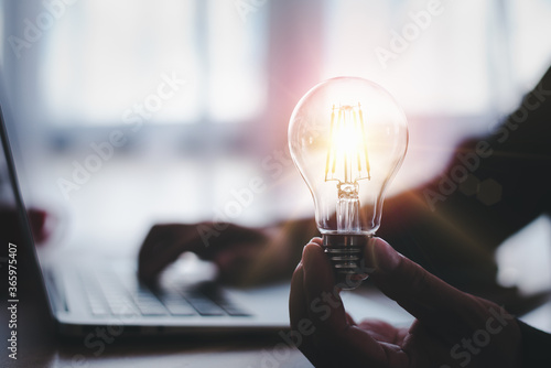 Fotomural hand of a man with a light bulb and he is using a notebook computer