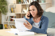 © PheelingsMedia - Serious adult woman checking letter calling on phone at home