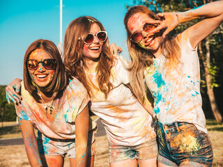 Three happy beautiful girls making party at Holi colors festival in summer time.Young smiling women friends having fun after music event at sunset. Positive models going crazy in sunglasses at sunset