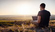 man with laptop sitting on the edge of a mountain with stunning views of the valley