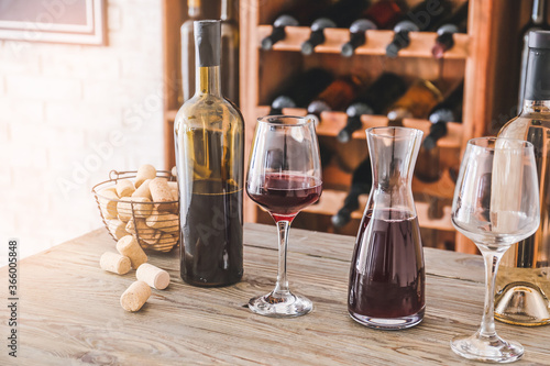 Fotografía Decanter with glasses and bottles of wine on table in cellar