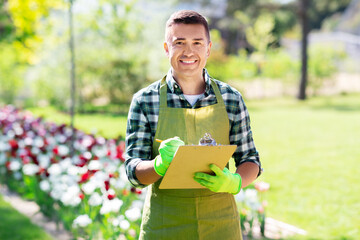 Wall Mural - gardening and people concept - happy smiling middle-aged man in apron writing to clipboard at summer garden