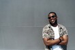 © Kateryna - Confident young afro-american stylish guy in sunglasses posing standing near a wall outdoors and smiling