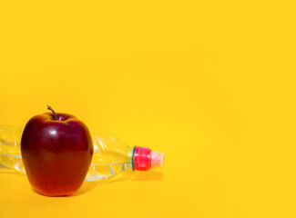 A red Apple lies on a yellow background next to a sports water bottle. Concept of proper nutrition, place for text