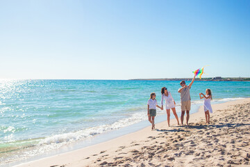 Wall Mural - Happy young family with two kids with flying a kite on the beach