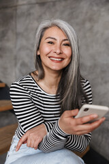 Canvas Print - Photo of happy adult asian woman smiling and using cellphone