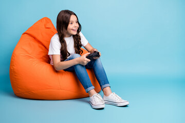 Portrait of her she nice attractive cheerful cheery focused wavy-haired girl sitting in bag chair playing online game isolated on bright vivid shine vibrant blue teal turquoise color background