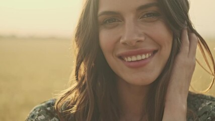 close up view of happy pretty woman wearing dress playing with her hair while posing on wheat field