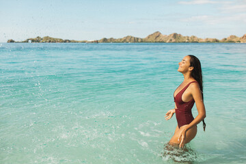 Young slim beautiful woman having fun and splashing water on beach with amazing transparent turquoise water. Leisure and relaxation. Wanderlust travel and vacations.