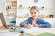 © Seventyfour - Portrait of cute girl smiling at camera while doing homework or tests sitting at wooden desk in cozy home interior, copy space
