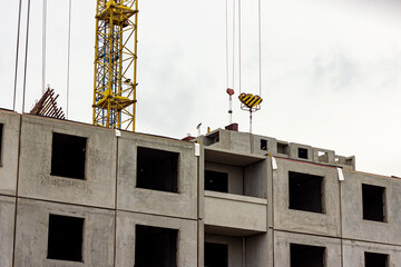 Construction site with the high crane building a grey block house in the city.