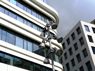 Wall Mural - Modern style street lights on steel pole with modern office buildings in the background in glass and aluminum cladding. pale gray and blue sky. modern architecture concept. reflecting sky in the glass