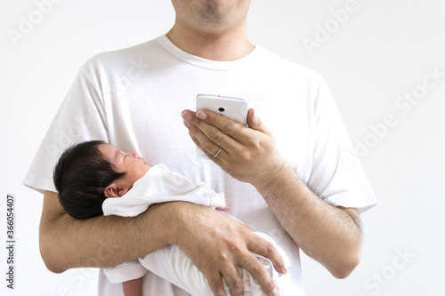 生後18日の赤ちゃんを抱いてスマートフォンを使う30代の男性 Stock Photo Adobe Stock 生後18日の赤ちゃんを抱いてスマートフォンを使う30代の男性 Stock Photo Adobe Stock
