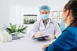 © DragonImages - General practitioner in medical mask filling document when taking to patient in his office