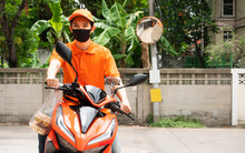 Asian Young Delivery Man Wear Face Mask Protect Covid-19 Or Coronavirus Disease And Orange Uniform With Cap Drive Motorcycle Transport To Send Fresh Food At Customer Home By Quality And Fast Service
