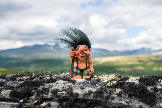 funny norwegian troll figure with big nose and walking stick outdoors in the mountains. hair standin