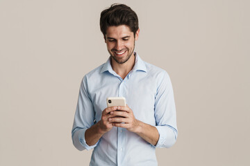 Image of happy man holding cellphone while standing by beige background