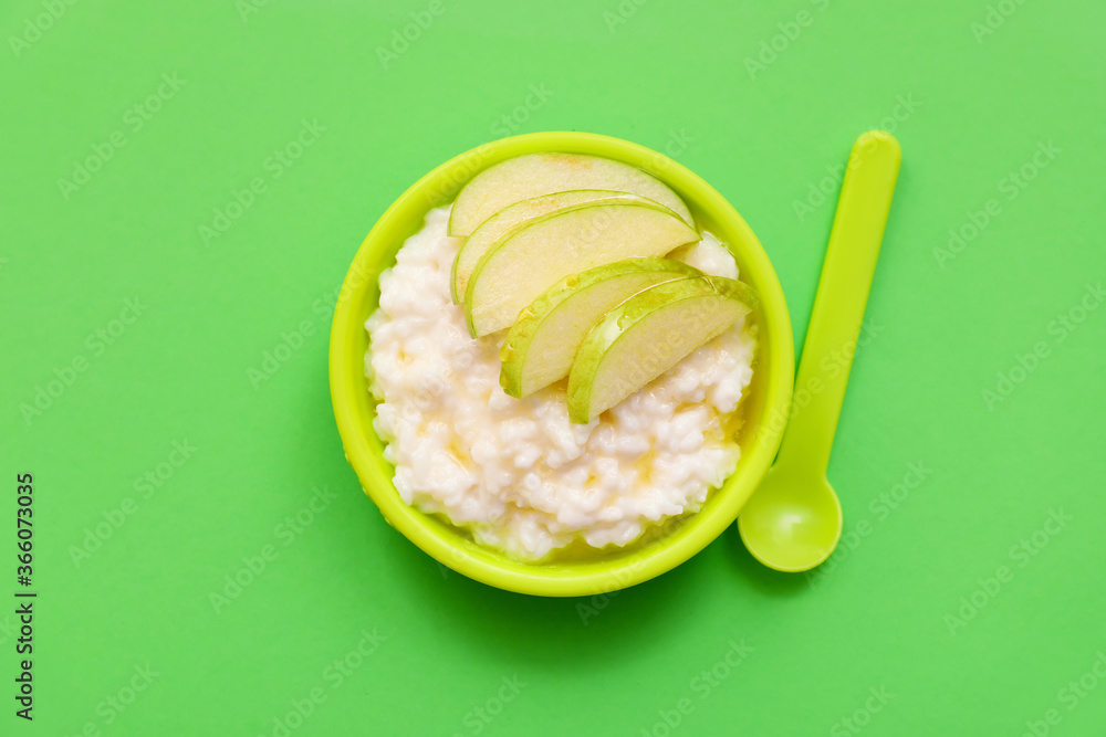 Plate with boiled rice and apple for child on color background