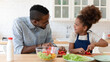 © fizkes - Loving happy biracial young dad teach little excited ethnic daughter cooking in morning at home, smiling african American father and small girl child prepare healthy organic vegetarian salad together