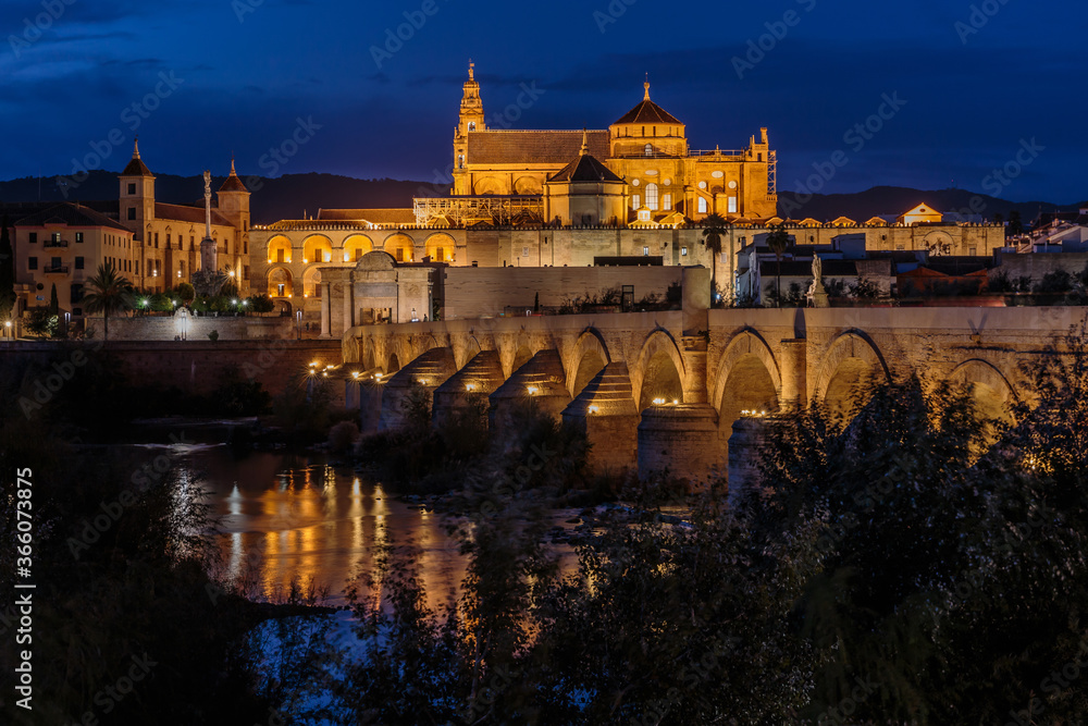 Cordoba old town in the evening at the blue hour. Mosque Cathedral with Roman bridge and river course. Illuminated buildings of the Spanish city in Andalusia - obrazy, fototapety, plakaty 