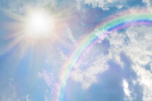 Summer Sun Burst And Blue Sky  Rainbow - Massive Sun Radiating Beside Fluffy Clouds With A Giant Arcing Rainbow And Beautiful Blue Summer Sky With Copy Space For Messages
