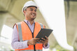 © Chanakon - Asian civil engineer operate with tablet to control working at construction. Worker wearing hard hat at highway concrete road site.