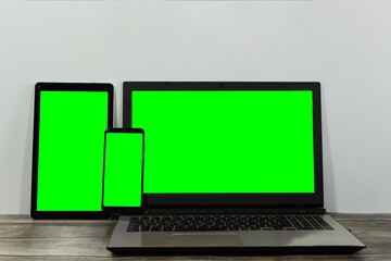 Wall Mural - Tablet, a laptop and a smartphone with green screens on wooden table