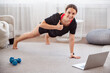 © Admiral - Happy fit woman showing thumbs up, doing plank exercises, during online workout on laptop, training in living room