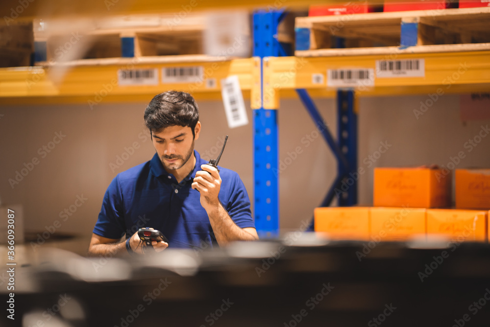 Male dispatcher, warehouse worker checking packages while using walkie-talkie in distribution warehouse storage. - obrazy, fototapety, plakaty 