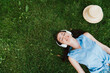 © LIGHTFIELD STUDIOS - top view of cheerful woman lying on grass and listening music near straw hat