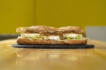 Sticker - Closeup shot of a sandwich with feta cheese and onions on a black round board on a wooden surface