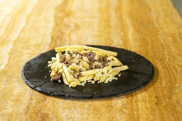 Canvas Print - Closeup shot of french fries with meat on a black round board on a wooden table