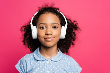 smiling curly african american kid in headphones isolated on pink