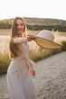 Young long-hair blonde who walks happily into the sunset. Girl in the country in summer with a dress and hat in hand 