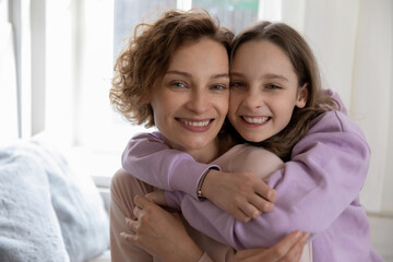 head shot portrait smiling teenage daughter hugging mother from back, overjoyed beautiful mum piggy 