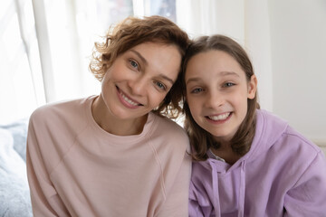 Head shot portrait smiling beautiful mother and teenage daughter looking at camera, posing for family photo, happy mum and pretty teenager girl making video call, shooting vlog together