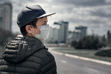 teenage boy poses in a city street, wearing a protective face mask - the concept of modern life and virus protection