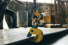 A Worker In A Factory Lifts A Bundle Of Sheet Metal Using A Crane And Mechanical Clamps. Metal Transportation At The Plant. Clamping Mechanism For Sheet Metal.