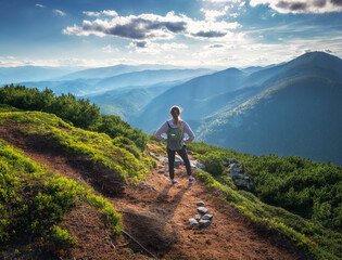 Wall Mural - beautiful mountains and standing young woman with backpack on the trail at sunset in summer. landsca