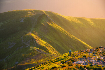 Wall Mural - Beautiful mountains in fog and standing woman with backpack on the mountain peak at sunset in summer. Landscape with girl on the trail, stones, green hills lighted by sunbeams. Travel and tourism