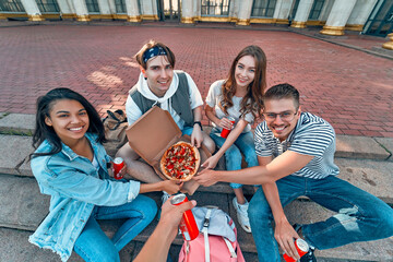 Wall Mural - A group of students sit on the steps outside the campus and eat pizza and soda. A group of friends are relaxing and chatting.