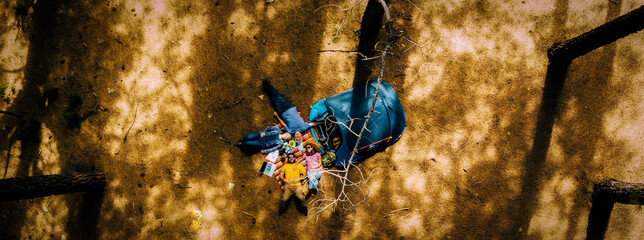 Vertical aerial view of group of friends enjoying the nature lay down on the ground with blue tent tiny home near for alternative vacation inthe forest