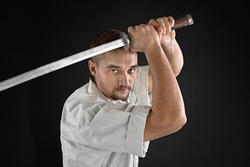 Portrait fighter master wearing traditional white kimono with steel samurai sword in hands. on black