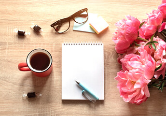 Still life on a table made of light wood. A white Notepad, a Cup of tea,, flowers.