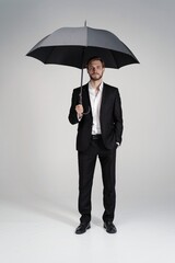 businessman in a suit standing under black umbrella